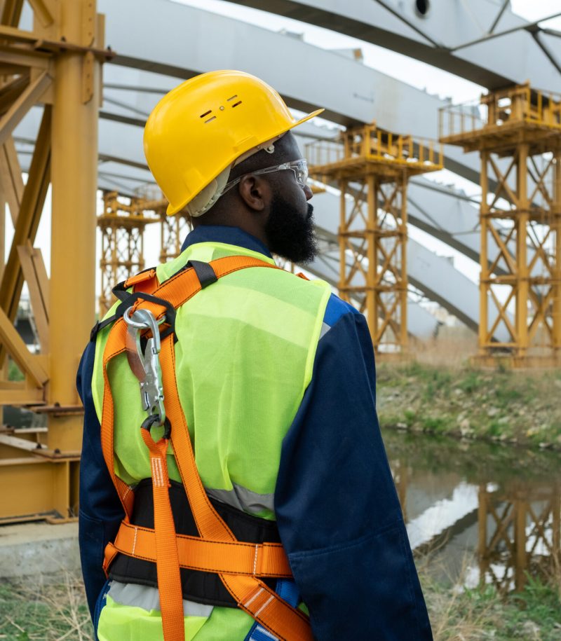 Young African engineer standing on construction site and looking at huge frames